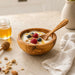 Wooden bowl with yogurt, berries, and granola on a light surface with honey and a towel.