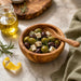 Wooden bowl with olives and feta cheese on a marble surface with olive oil and rosemary.
