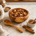 Wooden bowl filled with a mixed nut and seed trail mix on a marble surface with a wooden spoon and honey dipper.