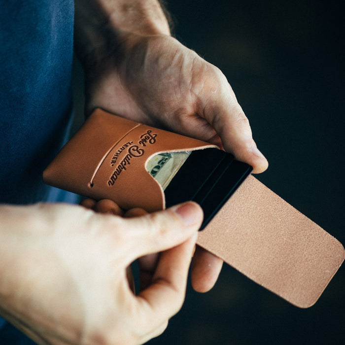 Brown leather wallet with card holder being held by a person against a dark background