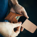 Brown leather wallet with card holder being held by a person against a dark background