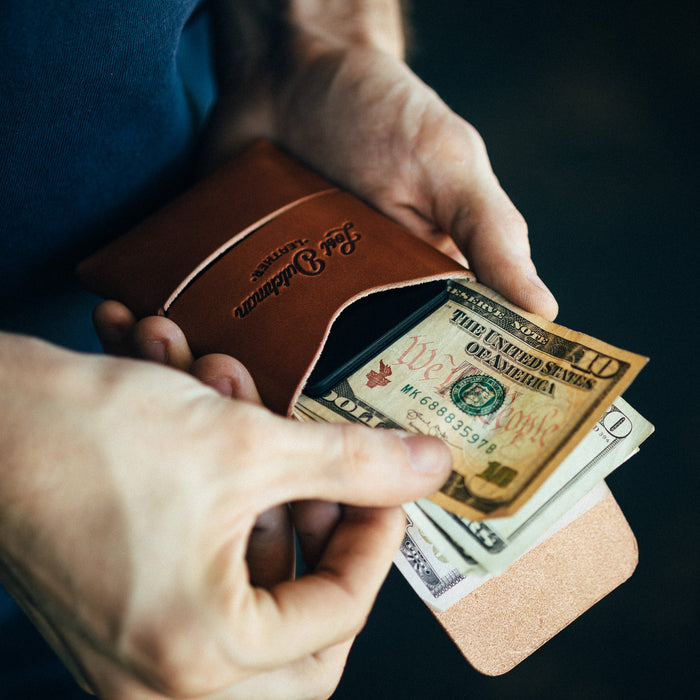 Person holding a leather wallet with US dollar bills