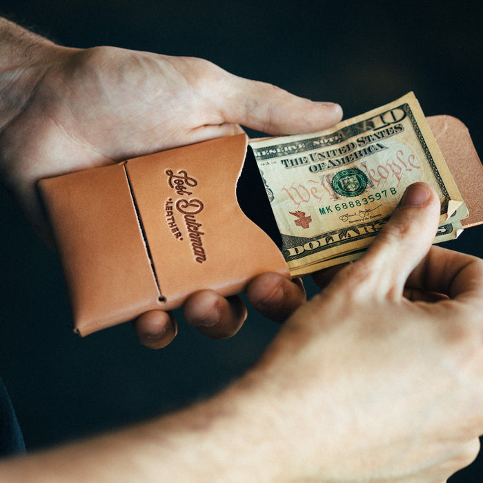 Person holding a brown leather wallet and a dollar bill against a dark background