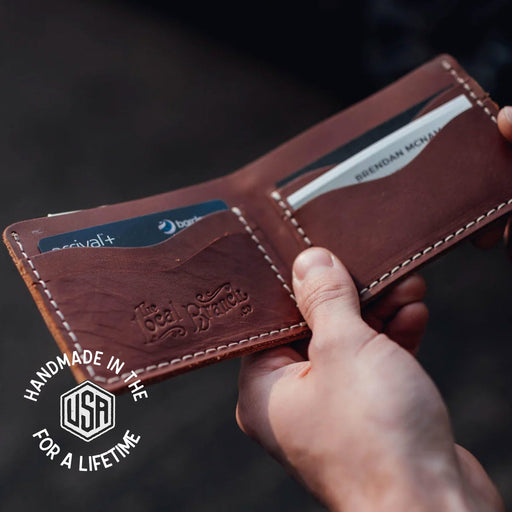 Brown leather wallet with 'Red Wing' branding held by a hand, against a dark background.