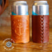 Two cans with leather sleeves on a wooden surface, featuring branding and 'Made in the USA' text.