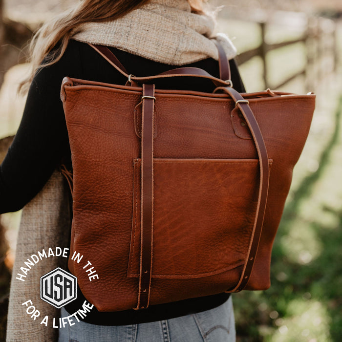 Person wearing a brown leather backpack with 'Handmade in the USA for a Lifetime' logo.