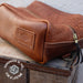 Brown leather toiletry bag with a visible brand logo on a wooden surface.
