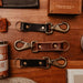 Three leather keychains with metal hooks on a wooden surface.