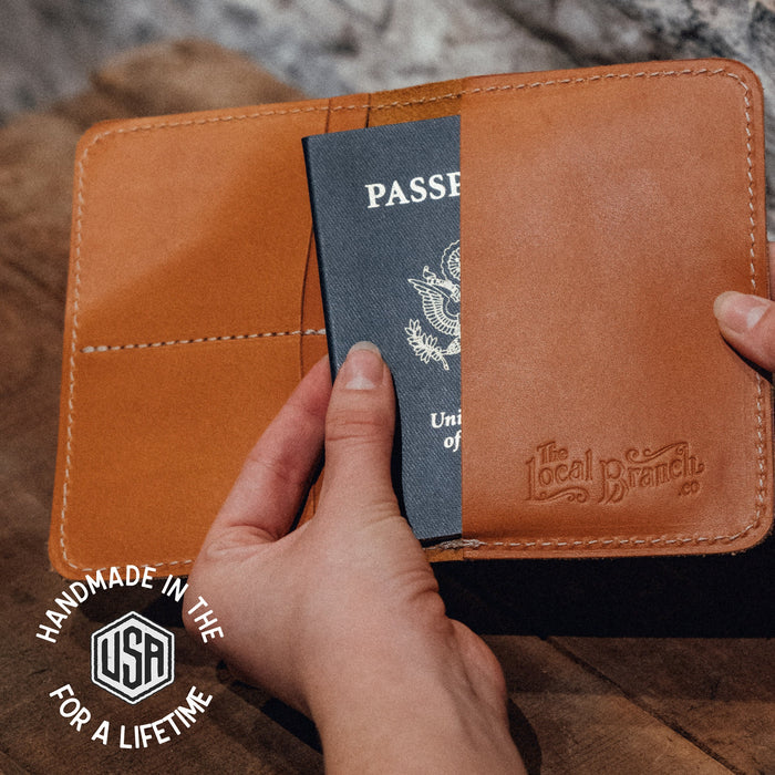 Brown leather passport holder with a passport inside, held by a hand on a wooden surface.