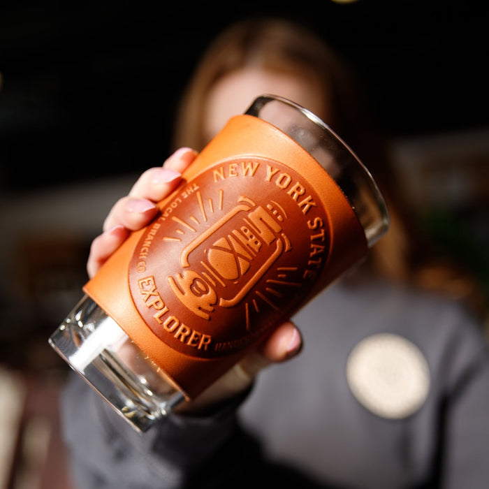 Person holding a glass with a leather cover featuring 'New York State Explorer' branding.