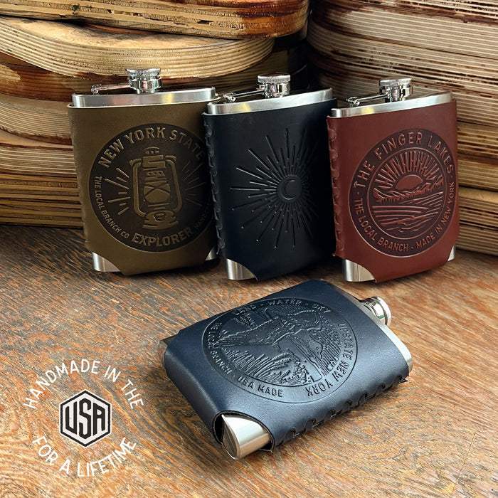 Four leather-flask set with embossed designs on a wooden surface, featuring 'Made in the USA' label.