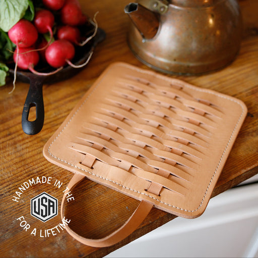 Brown woven trivet on a wooden surface with a copper kettle and radishes in the background.
