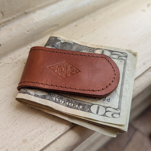 Brown leather money clip holding U.S. currency on a wooden surface