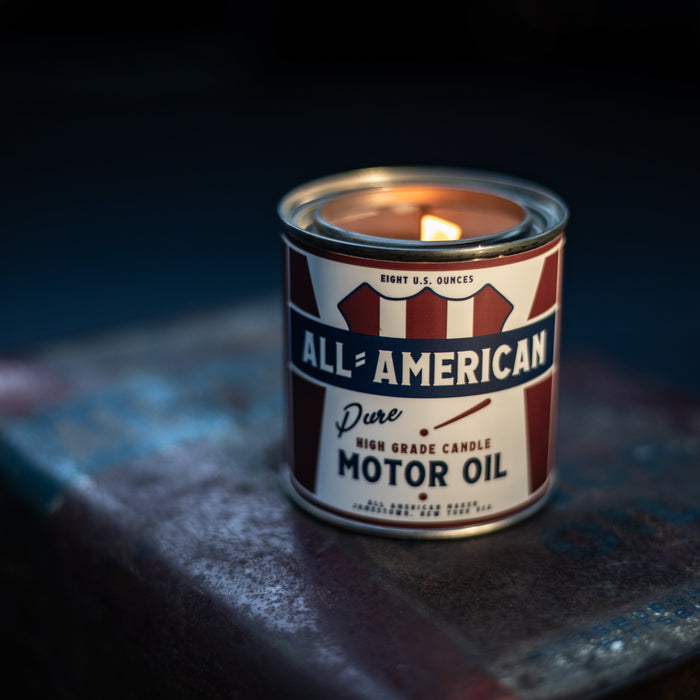Candle inside a can labeled 'All-American Pure Motor Oil' on a dark surface.