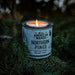 Candle in a container labeled 'All American Maker Northern Pines' on a branch with a dark background