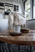Candle labeled 'All American Made Northern Pines' on a wooden table with a macrame chair in the background.