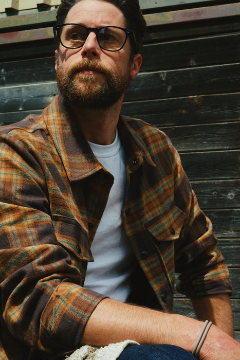 Man wearing glasses and a plaid shirt against a wooden background