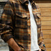 Person wearing a plaid shirt over a white t-shirt with a wooden background