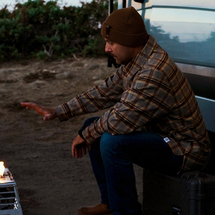 Person sitting by a small fire outdoors next to a vehicle