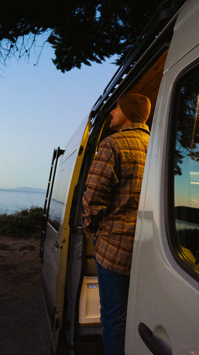 Person standing by a white van with open door, looking out at a scenic view.