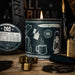 Candle with branding and illustrations on a wooden surface with tools in the background