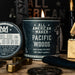 Candle labeled 'All American Maker Pacific Woods' with solid cologne and other items on a wooden surface.