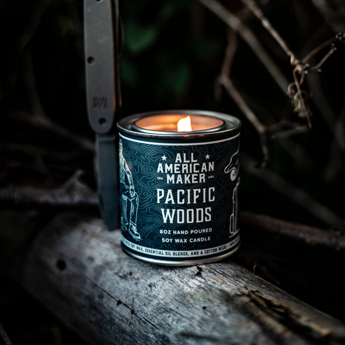 Candle in a 'Pacific Woods' container with a knife on a wooden surface