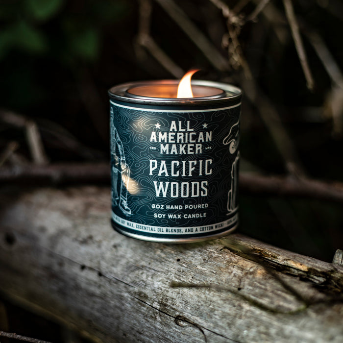 Candle in a can labeled 'Pacific Woods' on a log with a dark background