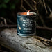 Candle in a can labeled 'Pacific Woods' on a log with a dark background