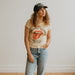 Woman wearing a graphic t-shirt and jeans standing on a wooden floor.