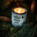 Candle in a tin labeled 'All American Maker Spruce Lake' surrounded by pine branches.