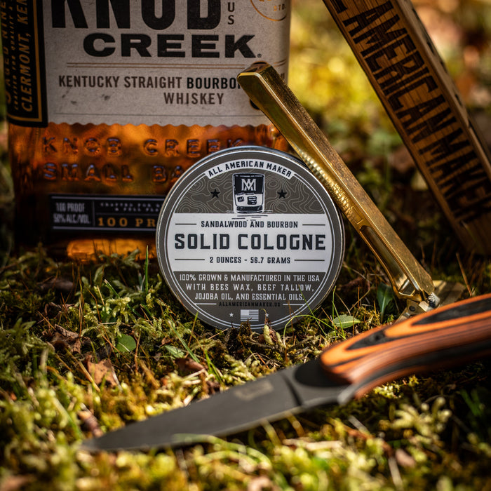 Knob Creek bourbon bottle, solid cologne, and knife on grass