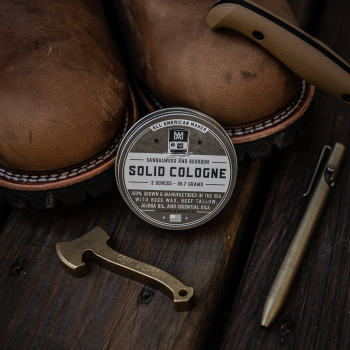 Solid cologne tin with leather boots and a knife on a wooden surface