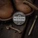 Solid cologne tin with leather boots and a knife on a wooden surface