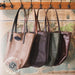 Three leather handbags hanging on a rack with a map background.