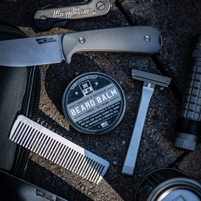 Collection of grooming tools including a knife, comb, and beard balm on a textured surface.