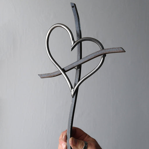 Hand holding a metal sculpture of two interlocking hearts against a gray background