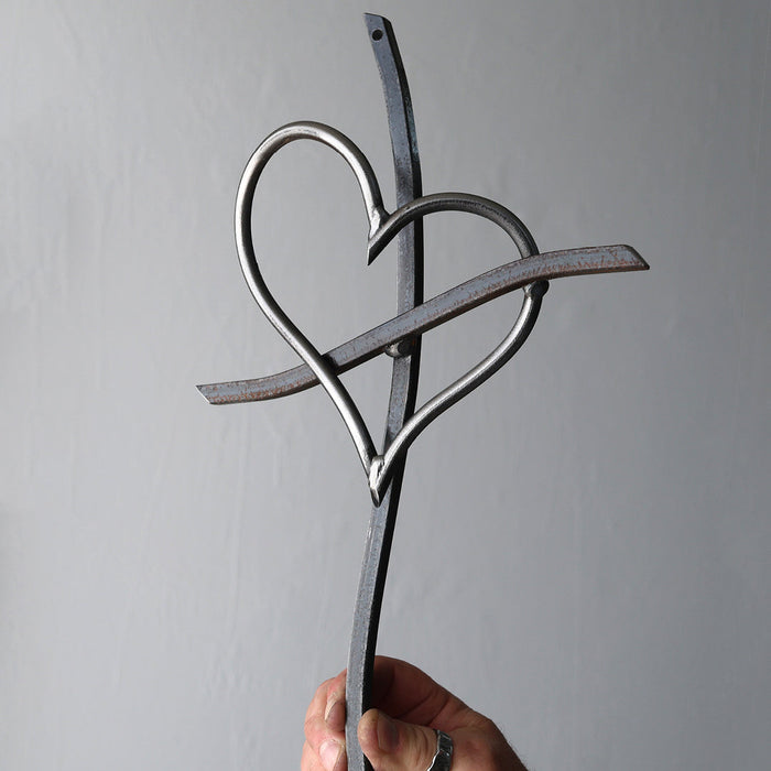 Hand holding a metal sculpture of two interlocking hearts against a gray background