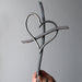 Hand holding a metal sculpture of two interlocking hearts against a gray background