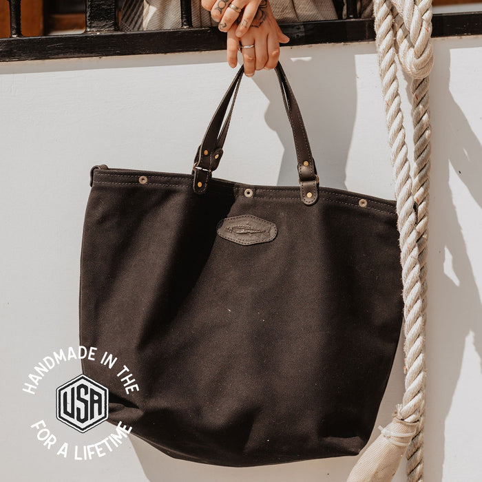 Black handbag held by a person with tattoos, hanging on a white wall.