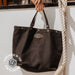 Black handbag held by a person with tattoos, hanging on a white wall.