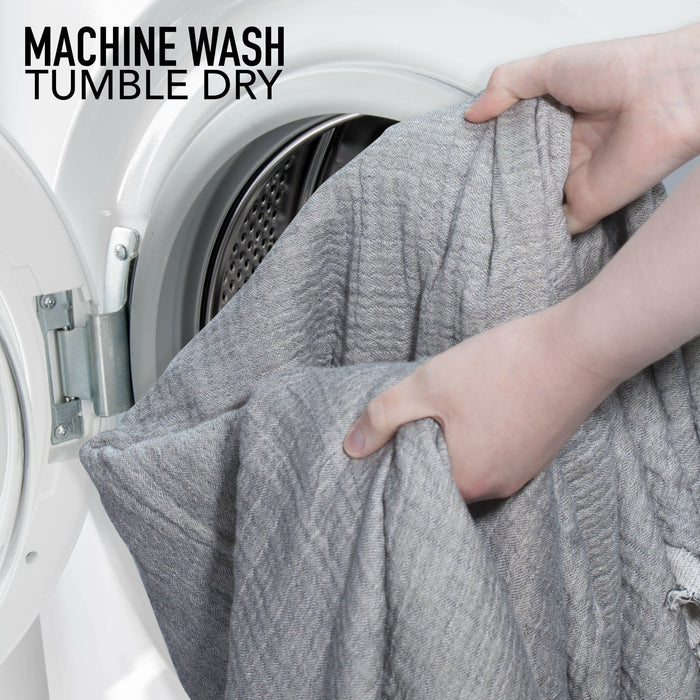 Person taking a gray towel out of a washing machine with text 'Machine Wash Tumble Dry'.