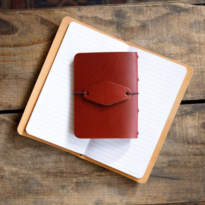 Red leather notebook cover on an open notebook with lined paper, on a wooden surface.