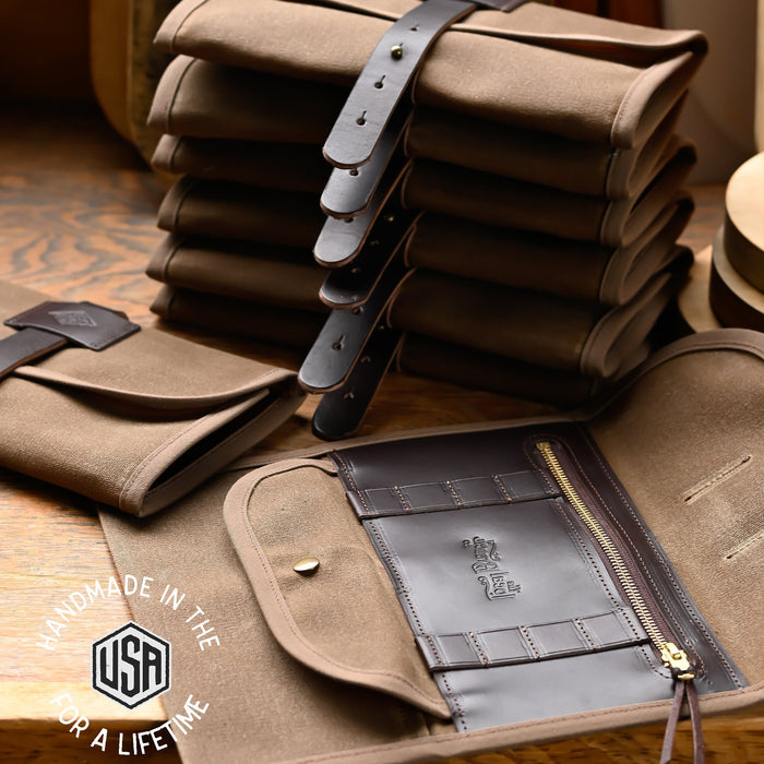 Stack of brown leather roll-up bags with visible 'Made in the USA' logo on a wooden surface.