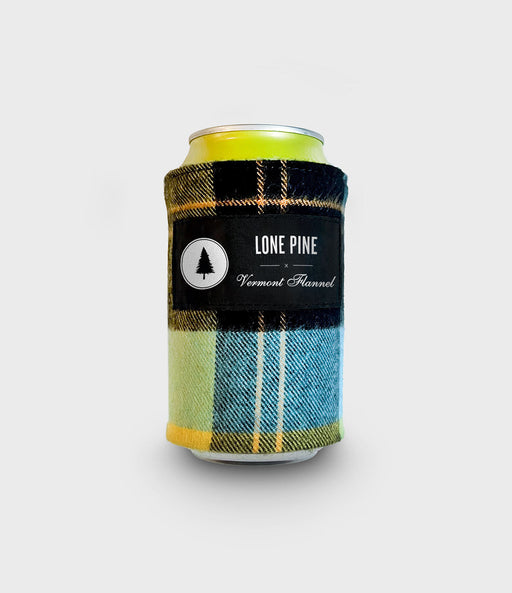 A beverage can wrapped in a plaid fabric can cooler sleeve. The sleeve features a black central band with the white text 'LONE PINE' and 'Vermont Panned' alongside a circular tree logo, with blue, yellow, and black plaid patterns on the sides, set against a light gray background.
