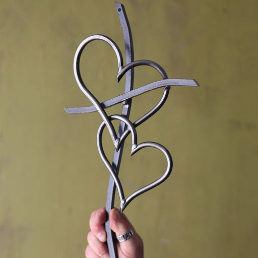 Hand holding a metal decorative item with heart shapes against a yellow background