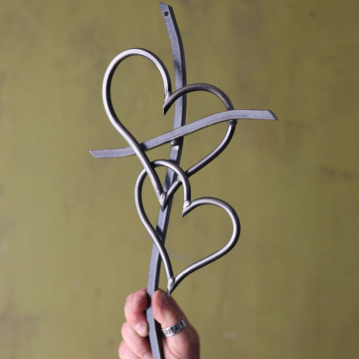 Hand holding a metal decorative item with heart shapes against a yellow background