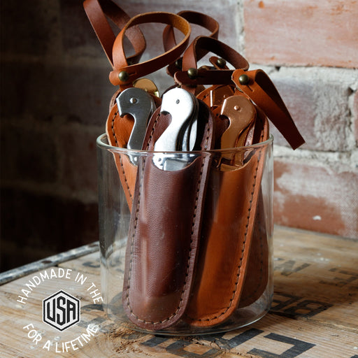 Set of leather gun holsters in a glass container with 'Handmade in the USA' label.