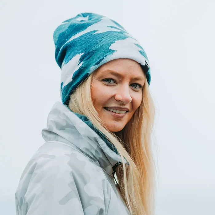 Person wearing a blue and white patterned beanie and light gray jacket against a light background