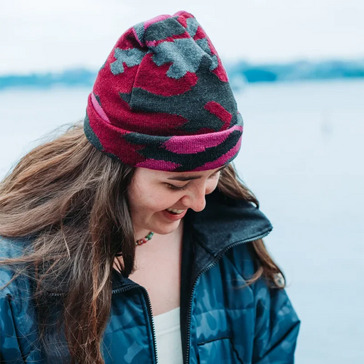 Person wearing a colorful knit beanie and blue camouflage jacket in a snowy landscape